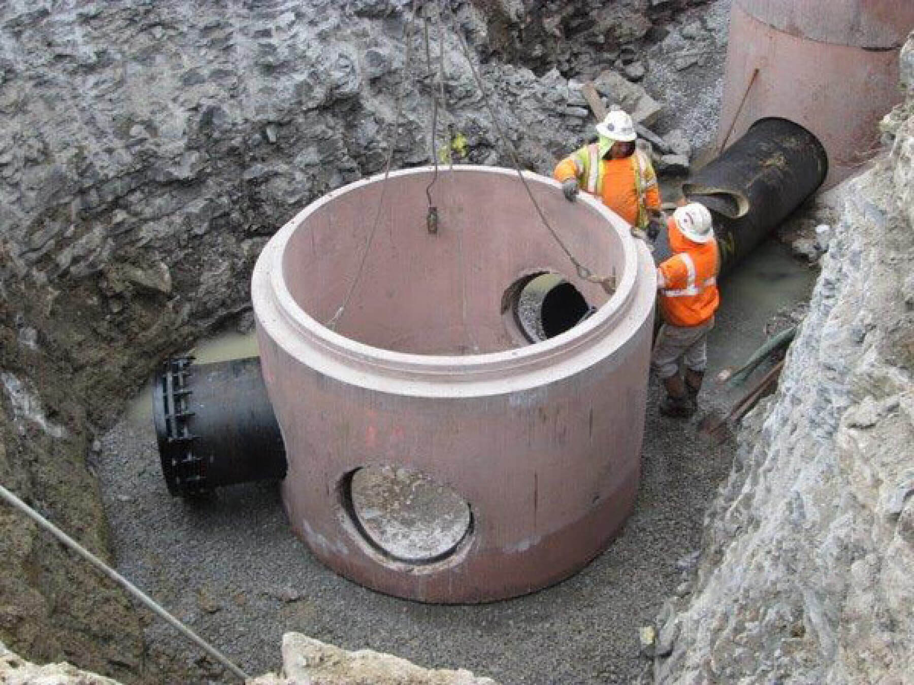 Workers secure a large section of pipe in a trench.