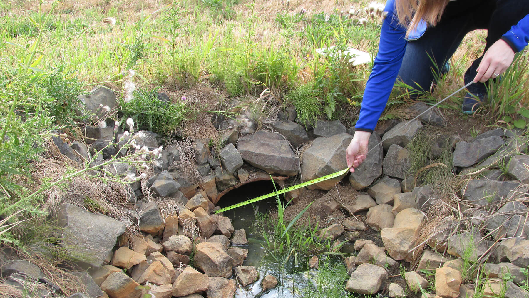 Person using tape measure at stormwater outlet