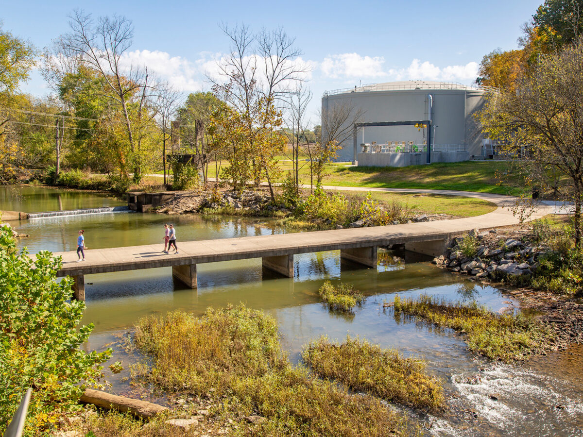 People walking over a bridge over a creek near a wastewater treatment plant