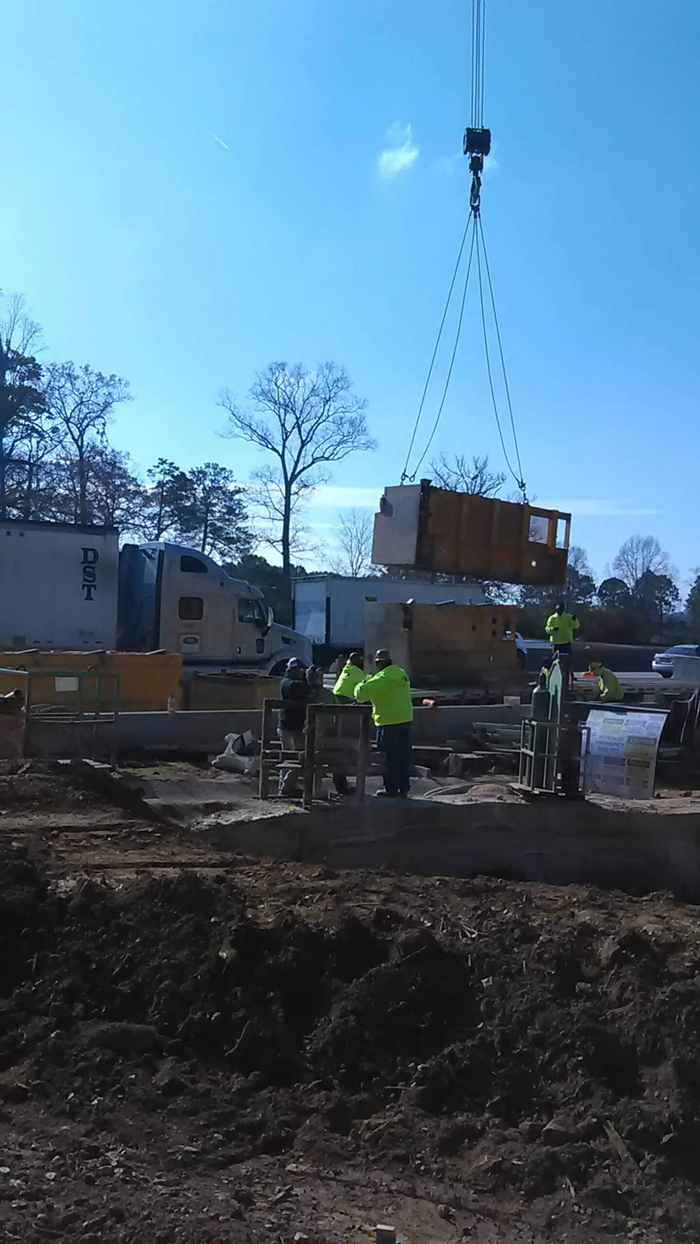 Workers assist a crane on a construction site.