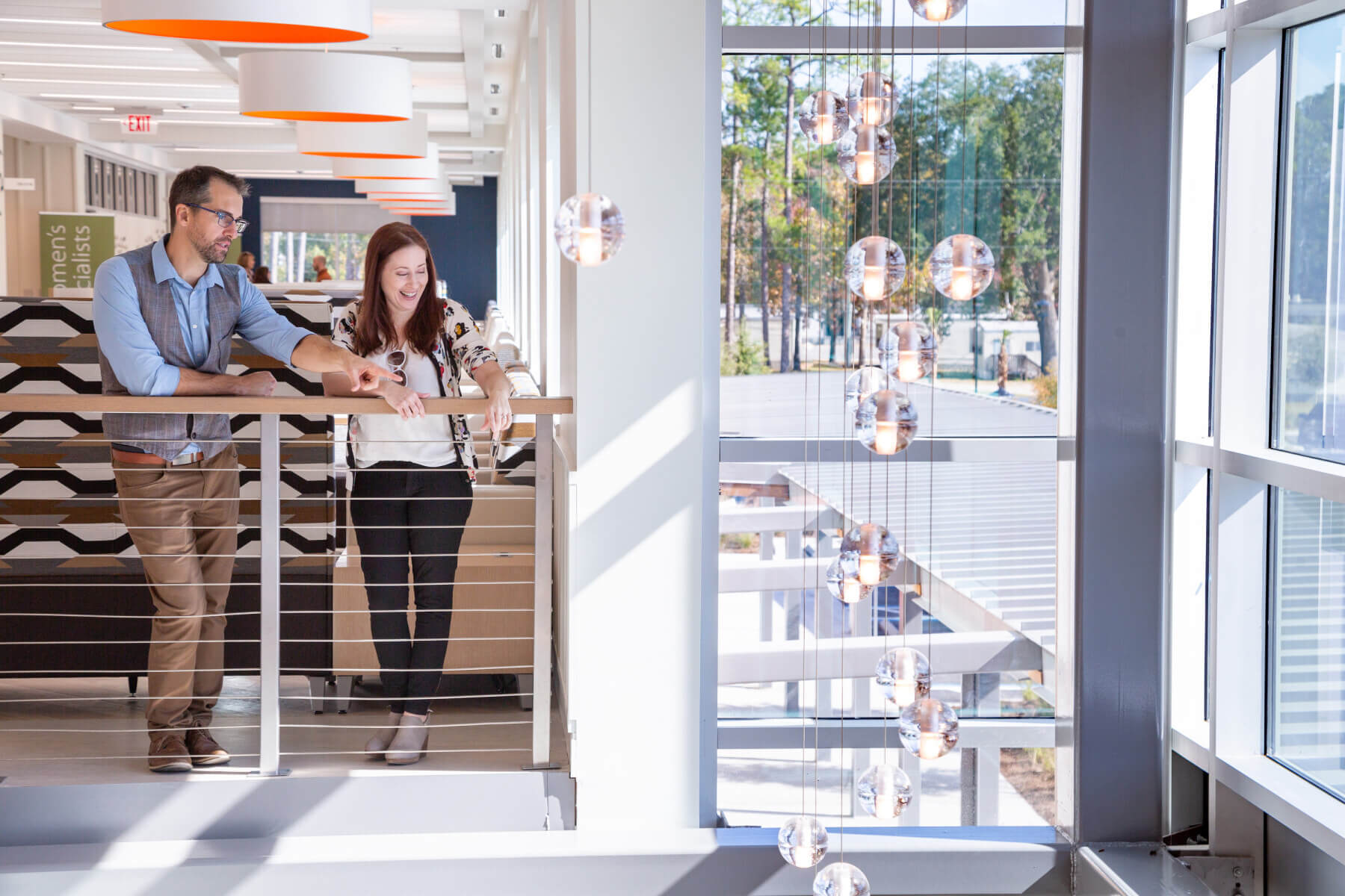 man and woman stand on balcony inside, looking out window