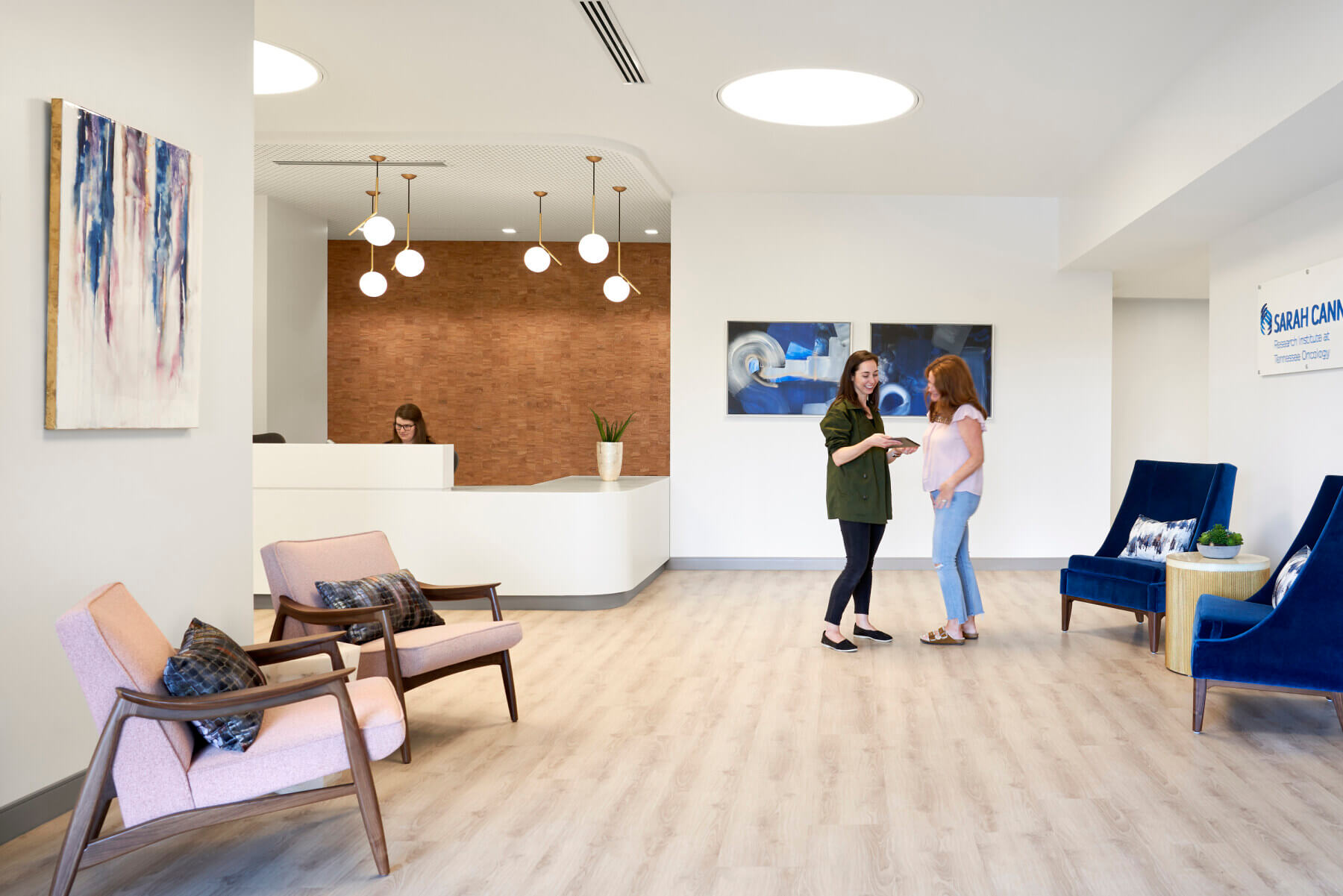 person sitting behind reception desk and two people standing in lobby