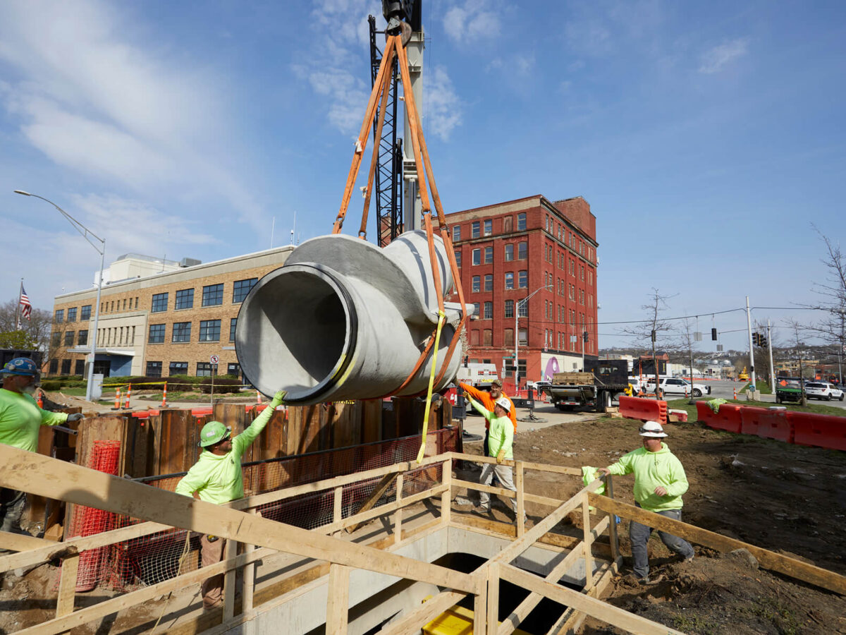 Portion of the concrete cylinder pipe being lowered by crane.