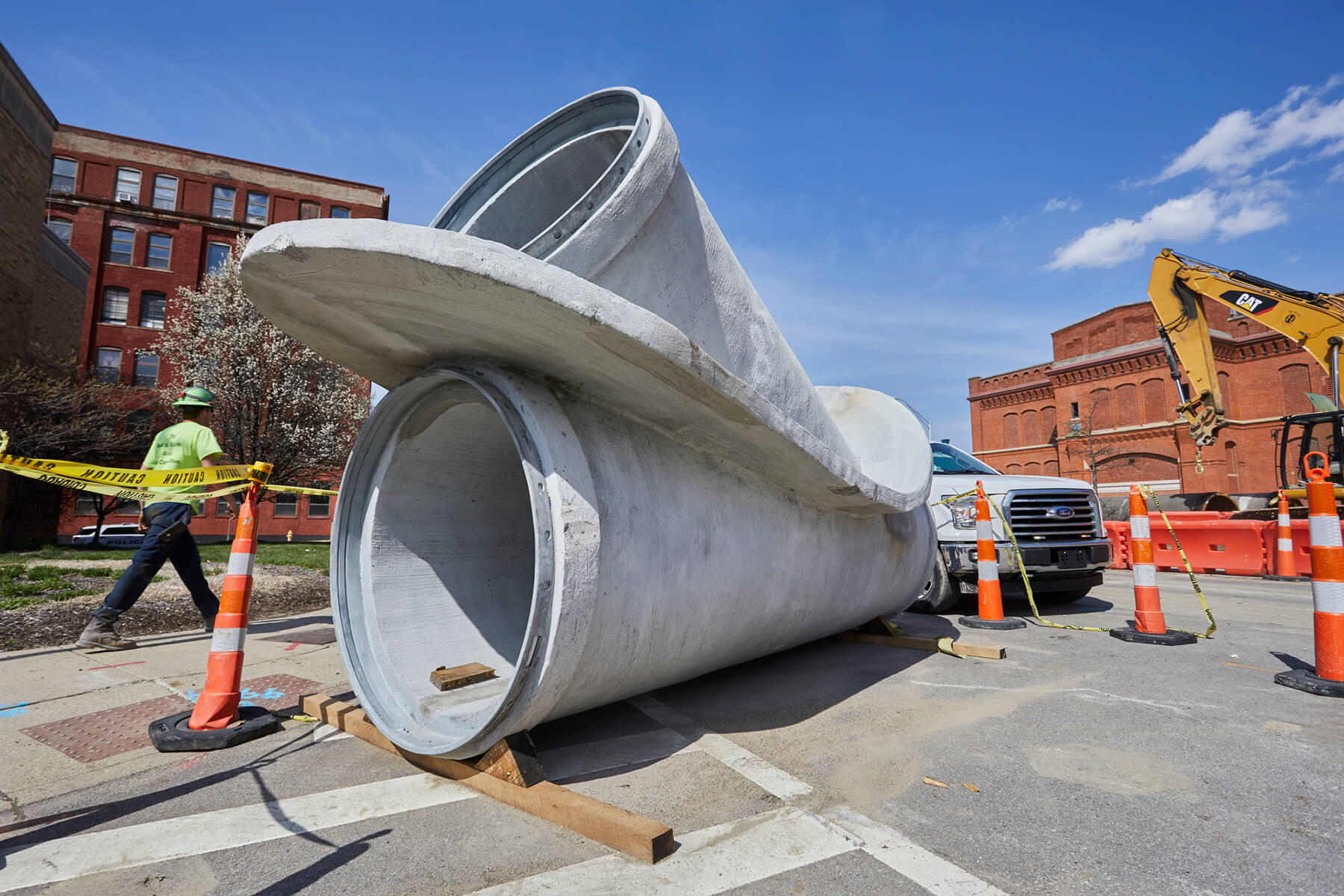 Section of pipe on sidewalk surrounded by cones.