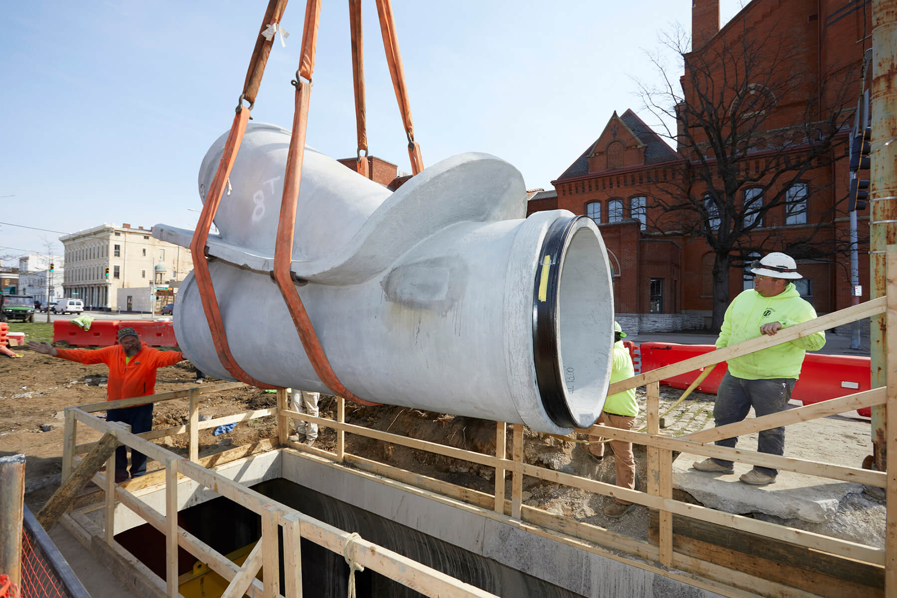 Workers look on as section of concrete pipe is lowered by crane.