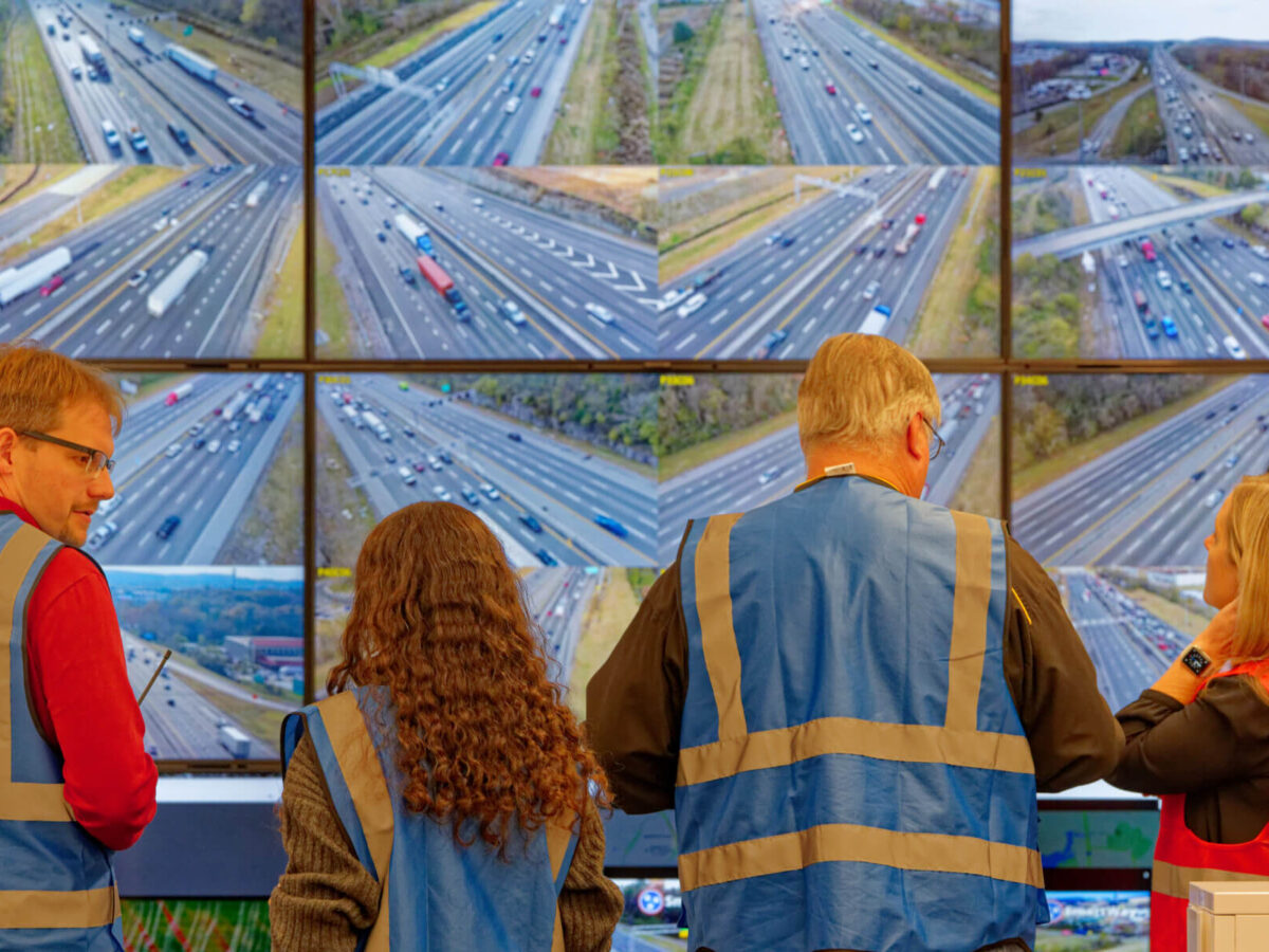 people looking at a screen with cars driving on the highway