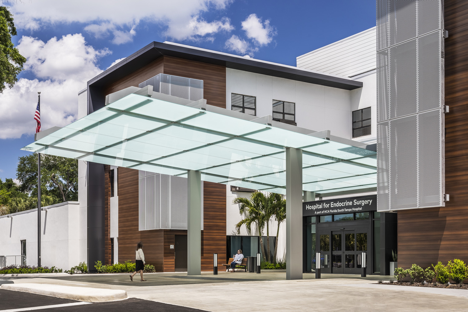 A person walking under a glass canopy outside a hospital