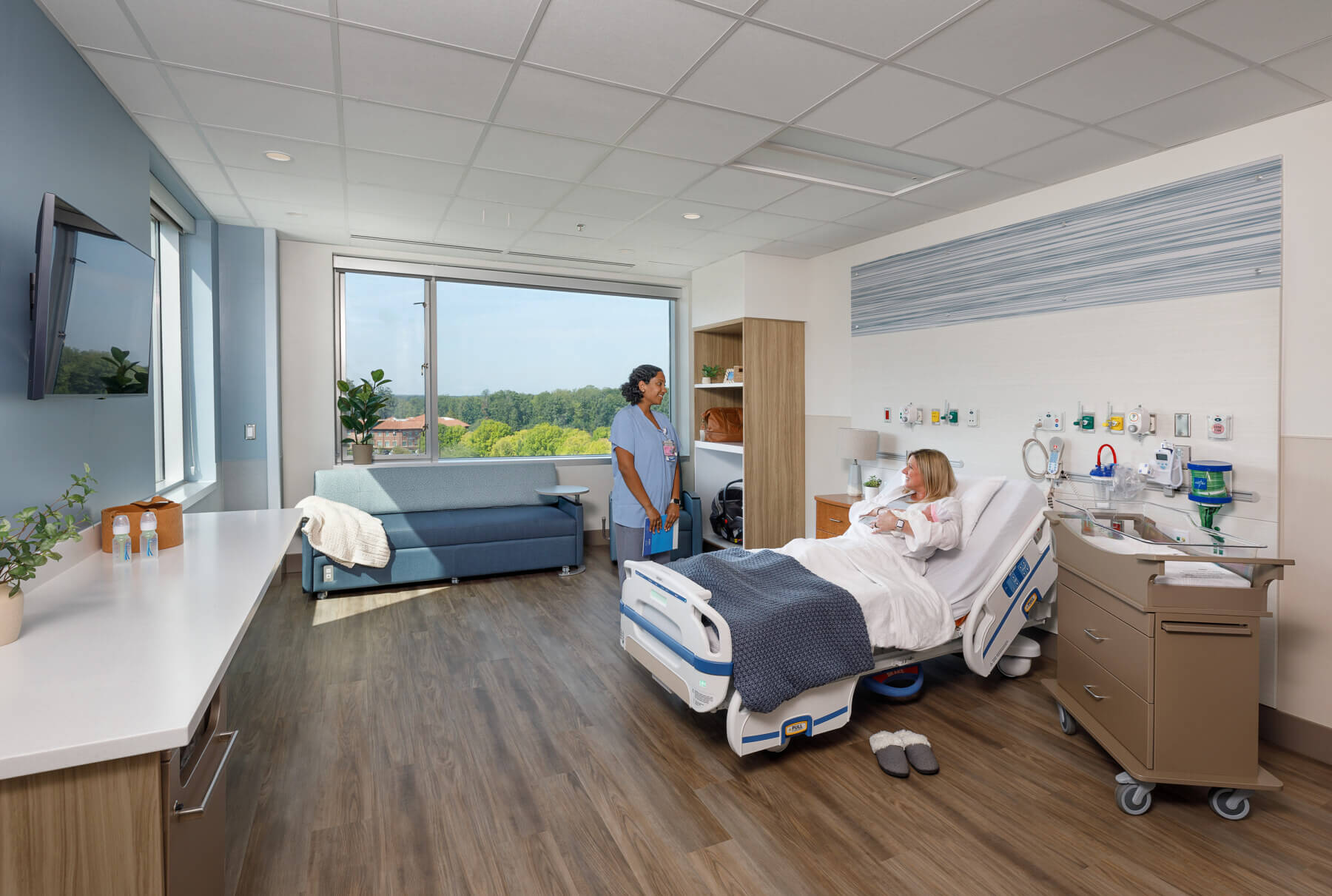 a nurse talking to a new mother sitting in bed holding a baby in a patient room