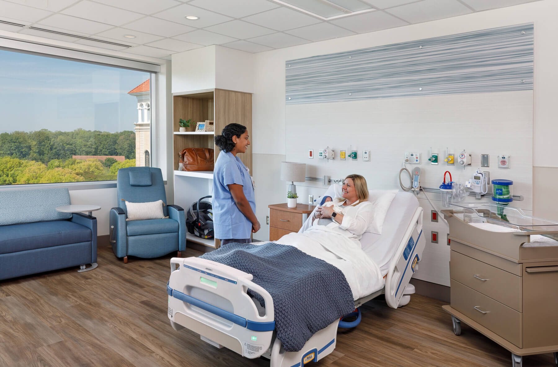 a nurse talking to a new mother sitting in bed holding a baby in a patient room