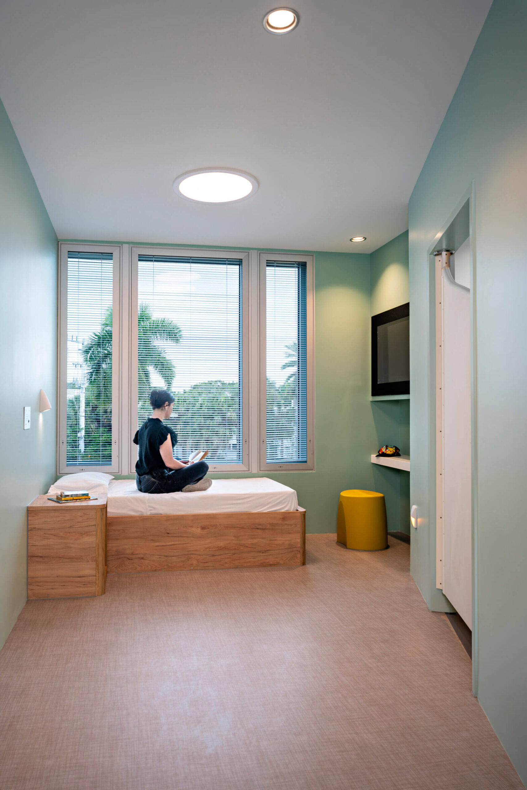 a patient sitting on their bed in their room at the behavioral health pavilion building at Sarasota Memorial Hospital