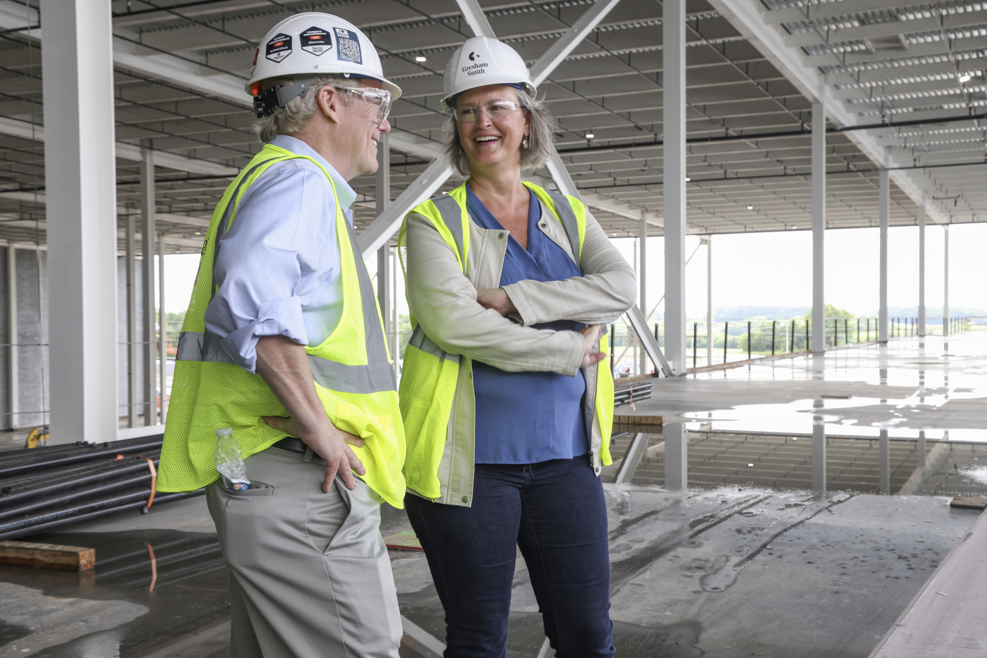 Two people wearing safety vests and hard hats talking while on a jobsite