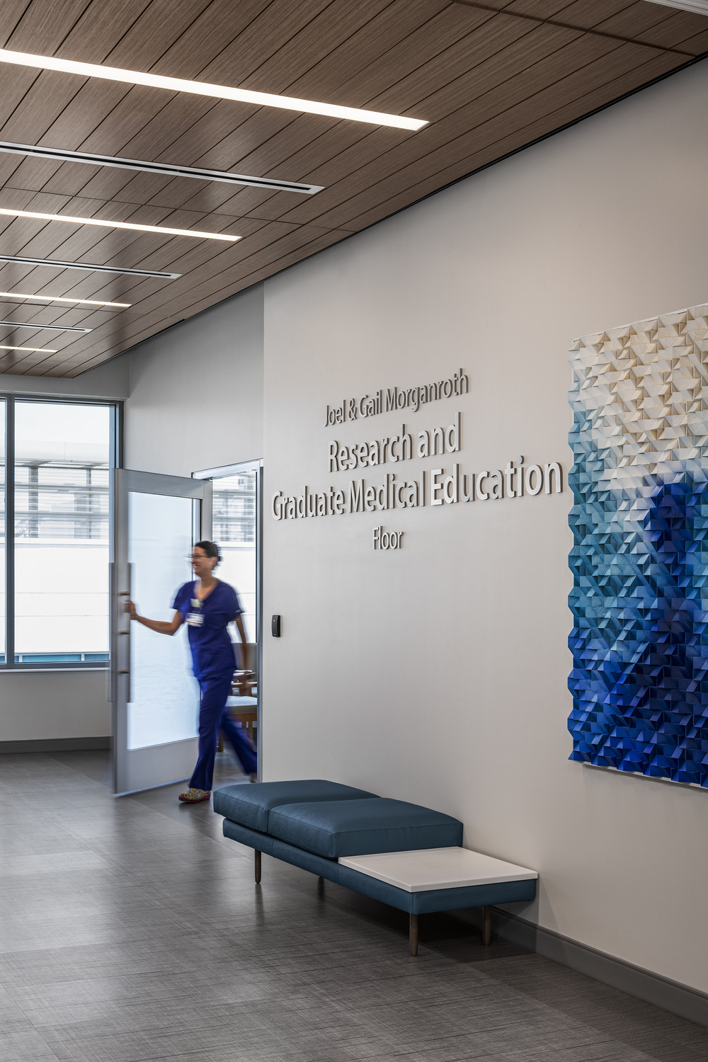 person exiting a room and entering a corridor with blue artwork on the wall