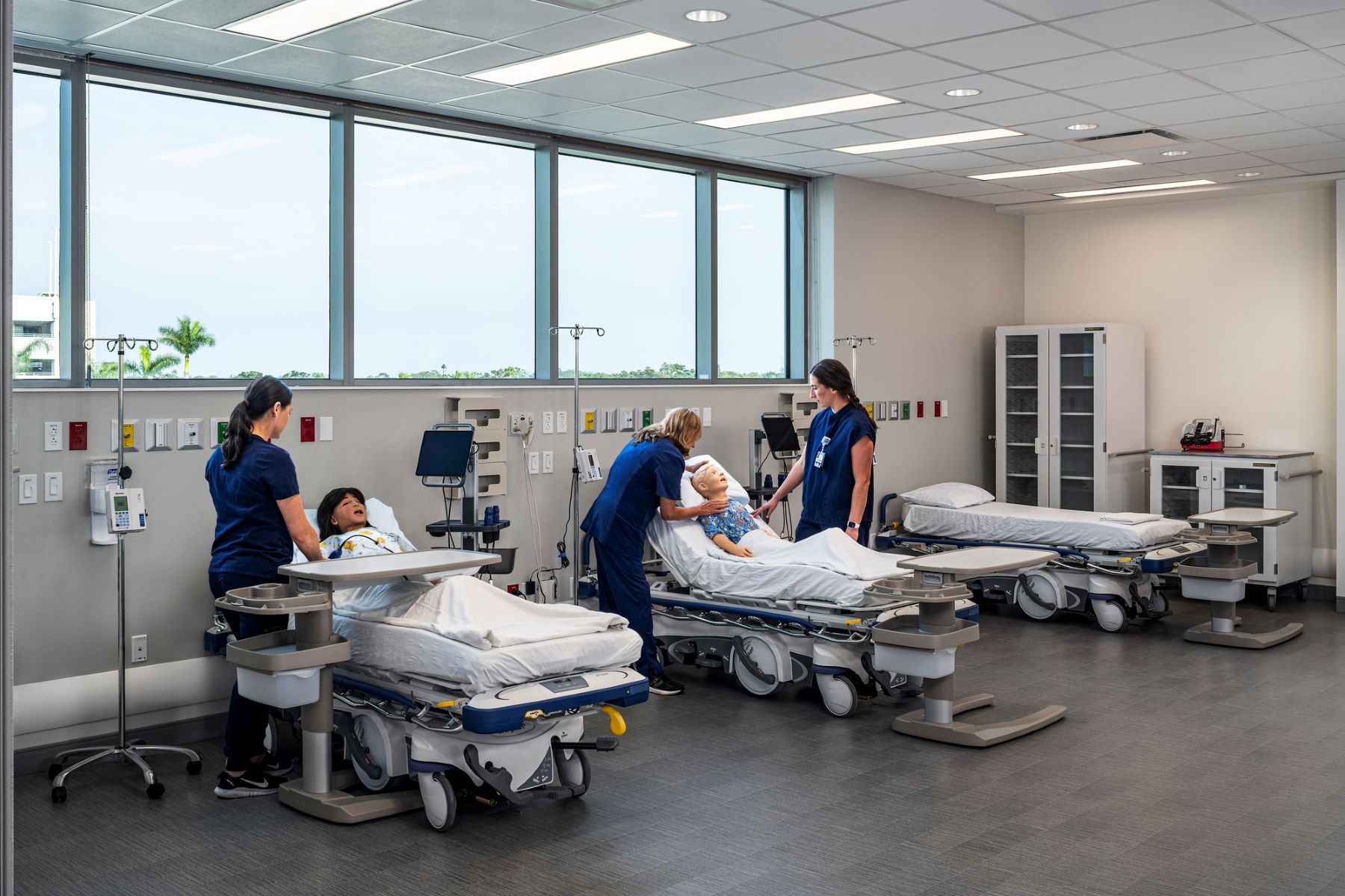 three medical students standing at the bedsides of simulation patients