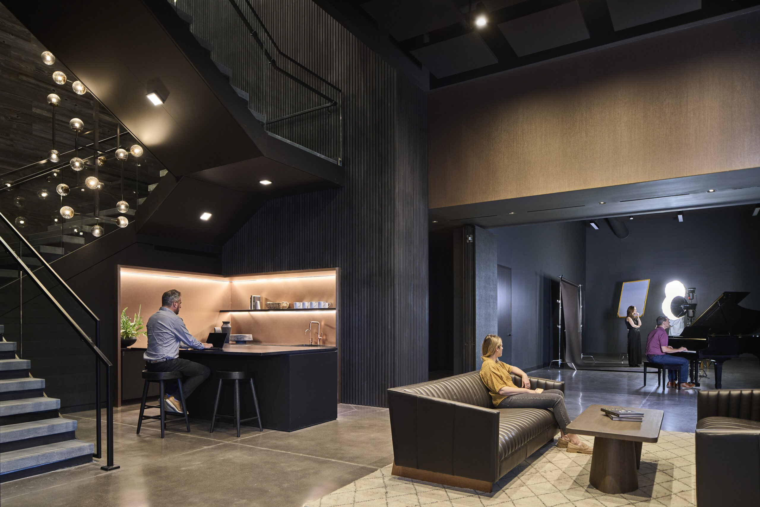 One person on a laptop at a bar, one person sitting on a couch, one person playing piano and two people take a photo in an office