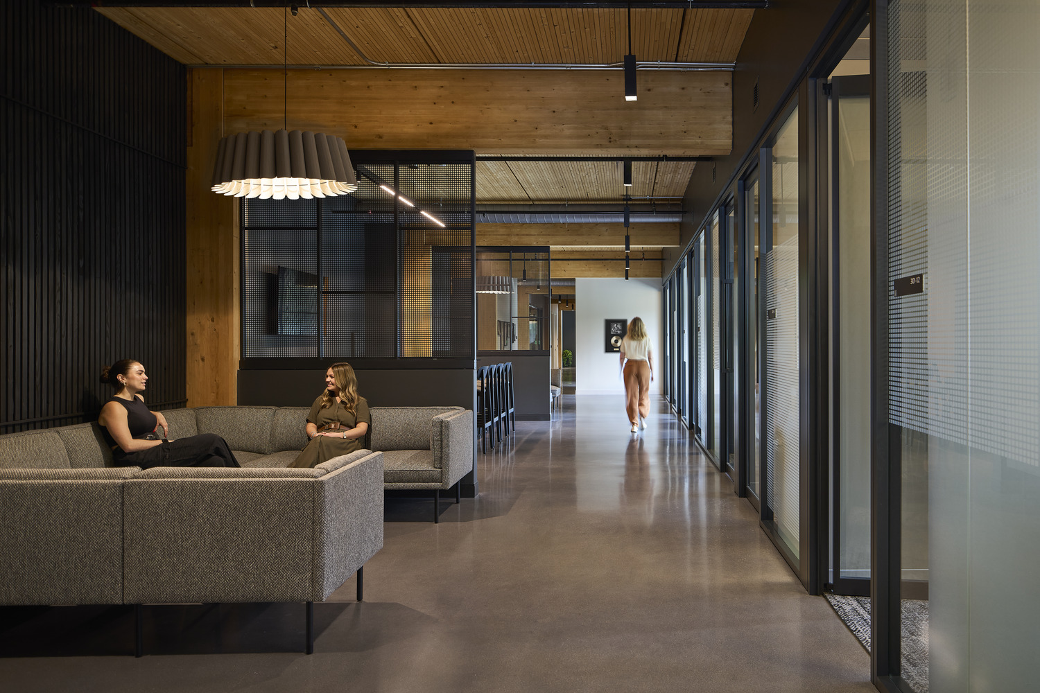 A long hallway in an office with one person walking and two people on a couch