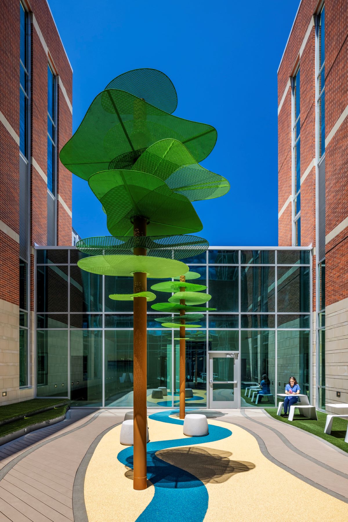 an adult sitting on an outdoor terrace next to a building with outdoor seating areas and fake trees