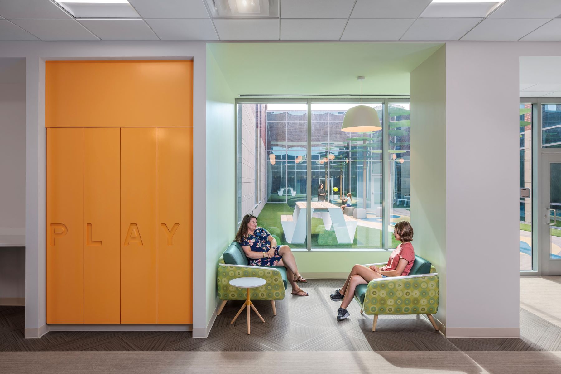 two adults sitting in chairs next to a window in a hospital waiting area