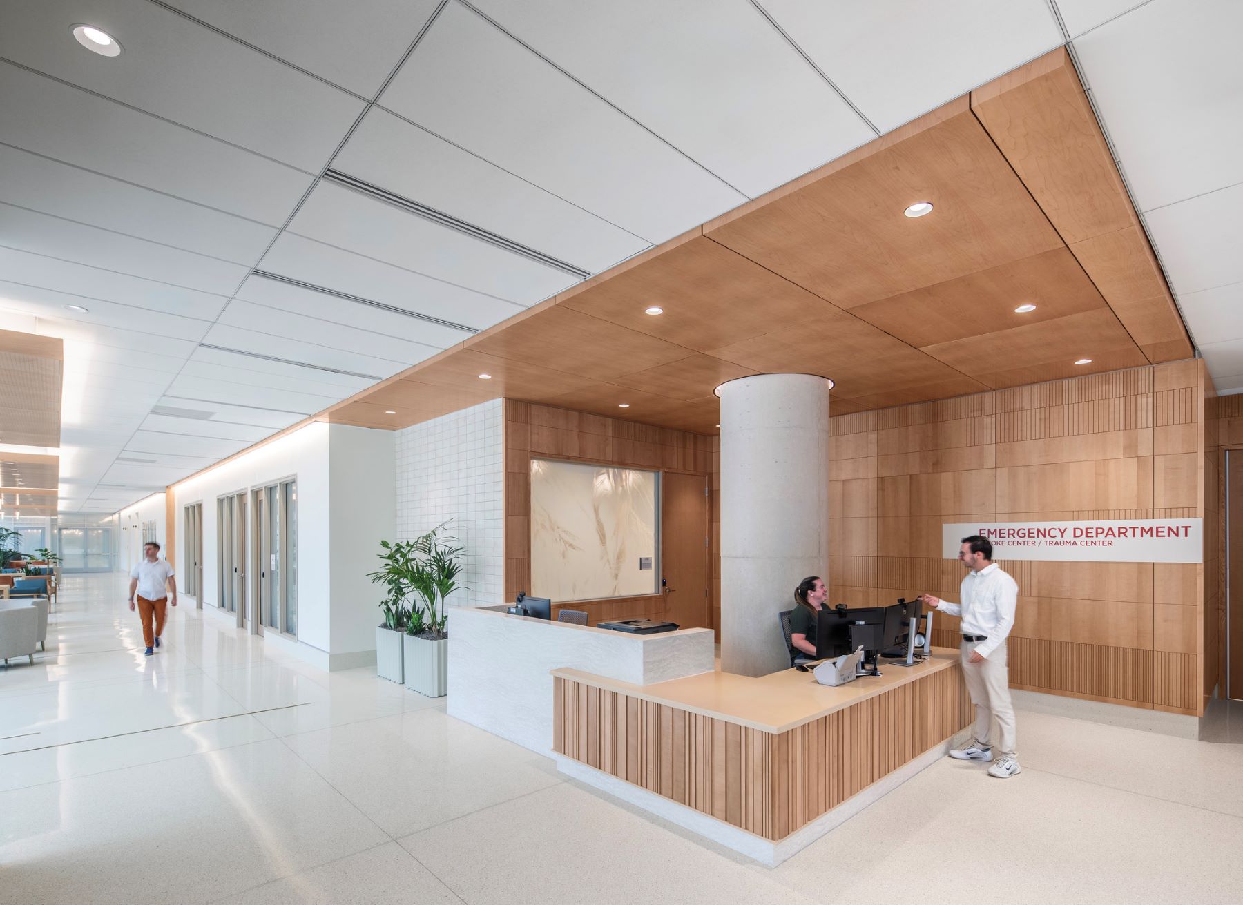 a person speaking to someone behind a reception desk in an emergency department in a hospital