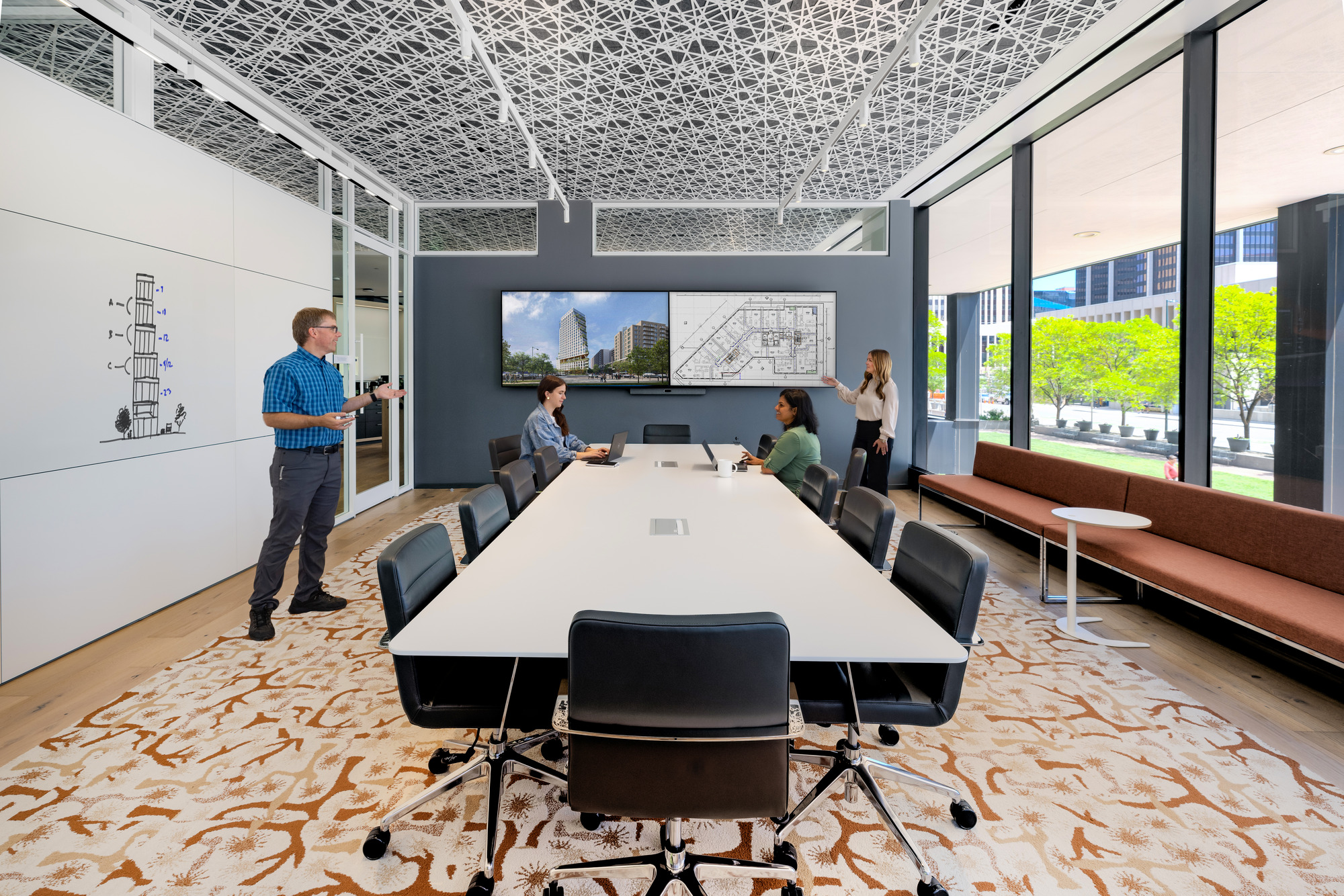 two people sitting at a long table and two people standing presenting in a conference room