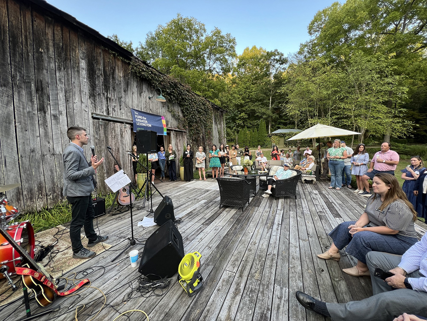 People standing on a wood deck listening to a man with a microphone