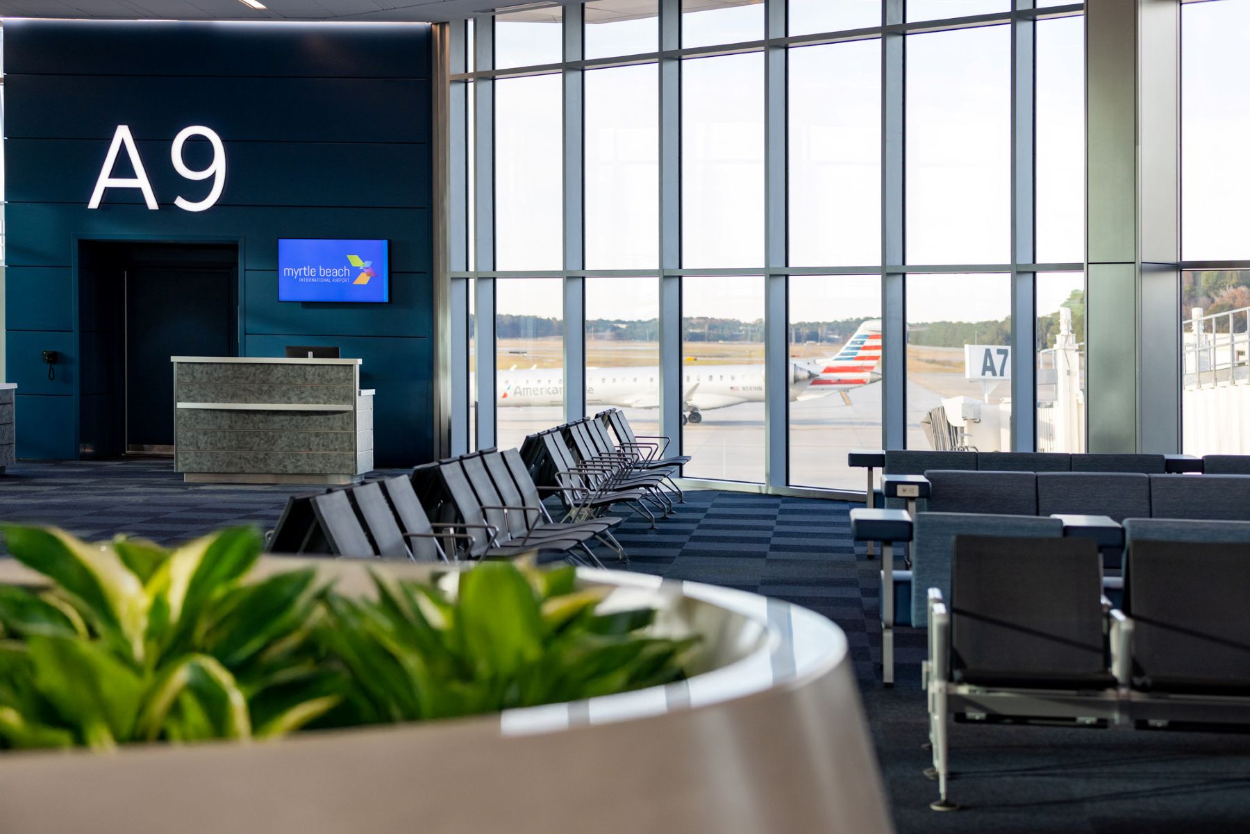 a planter and seating next to a wall of windows overlooking the tarmac at Myrtle Beach Airport