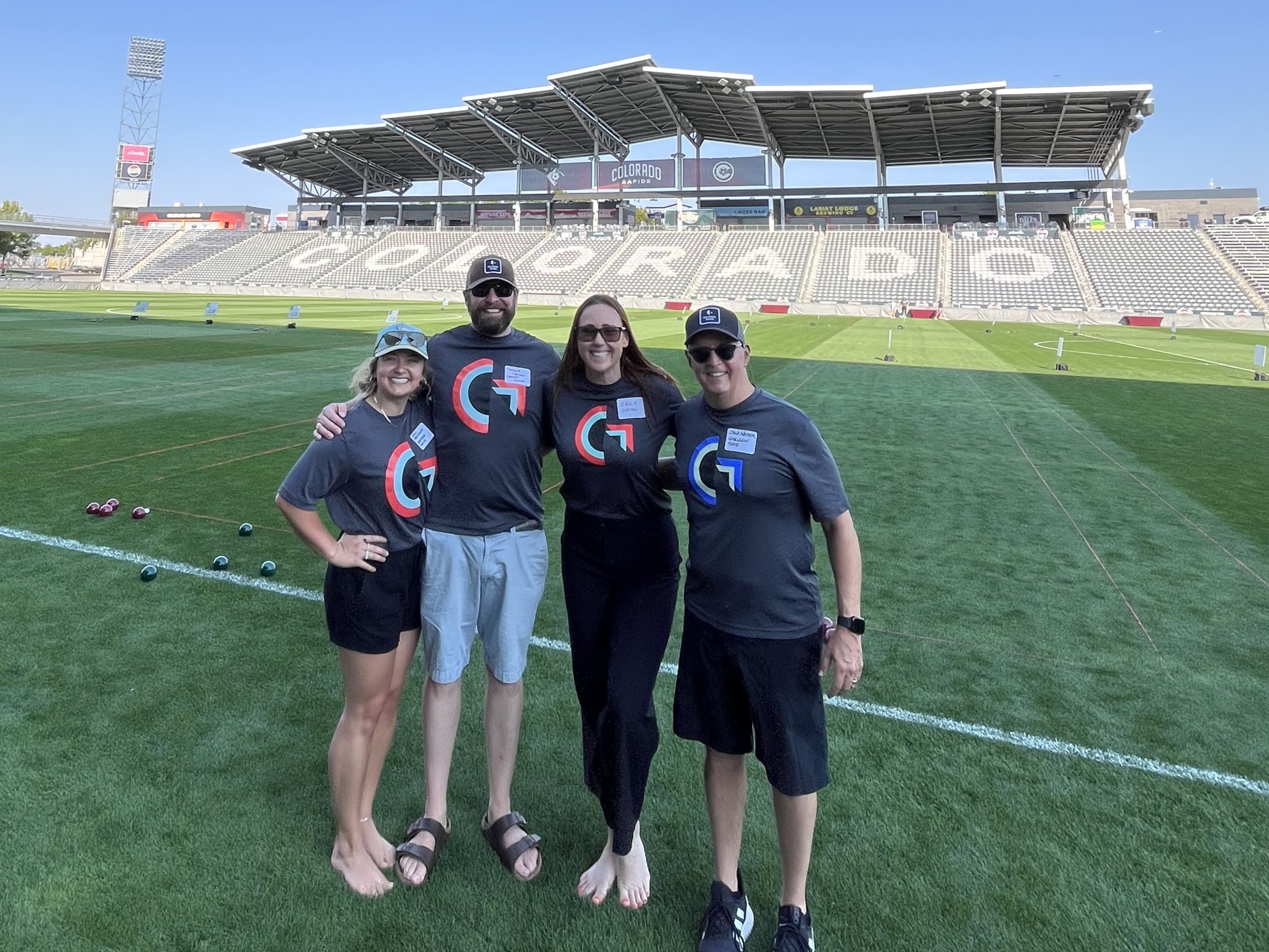 Four people standing on a soccer field in Denver, Colorado wearing grey shirts with the Gresham Smith logo on the chest